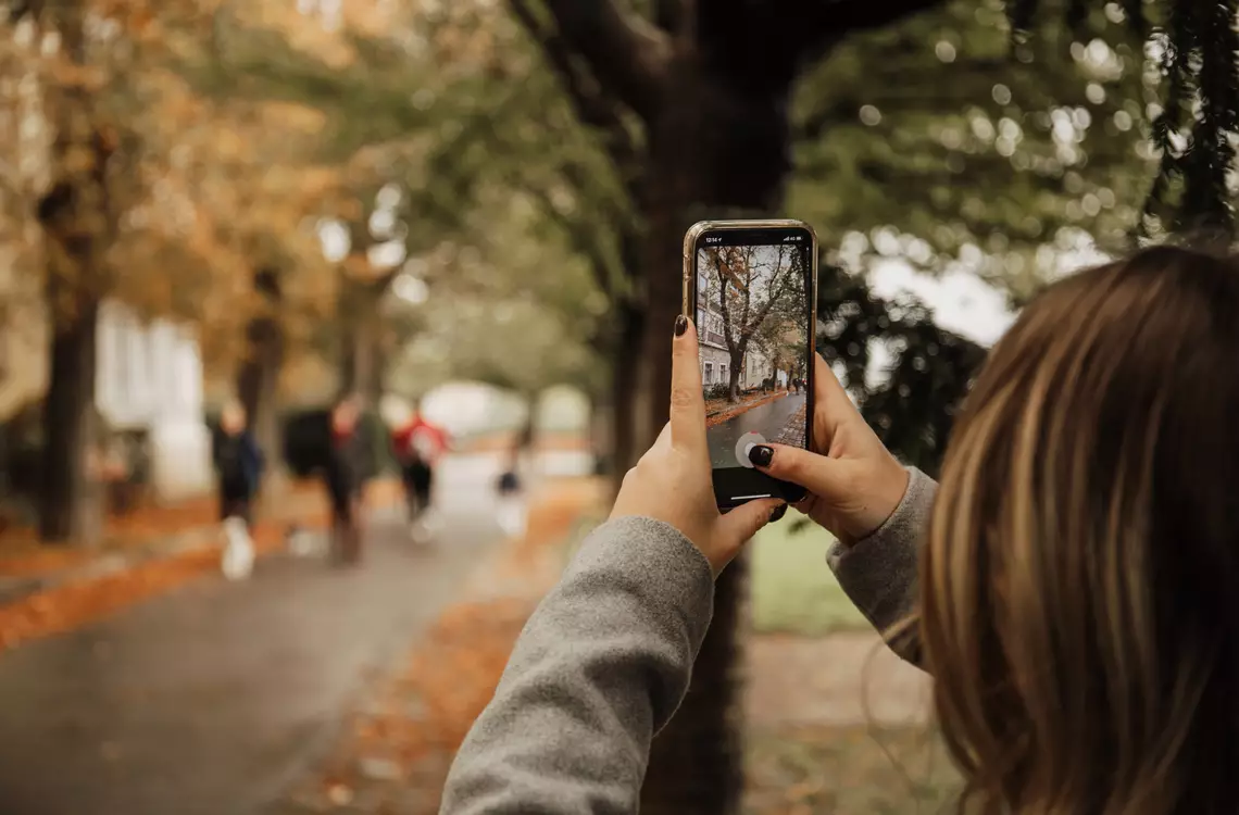 Une jeune fille prenant une photo avec son smartphone d'une rue fréquentée