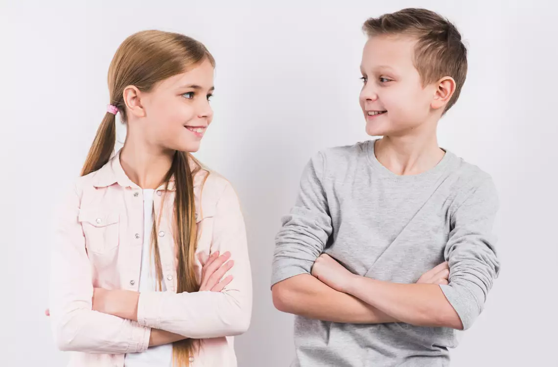 Une fille et un garçon se faisant face souriant et bras croisés
