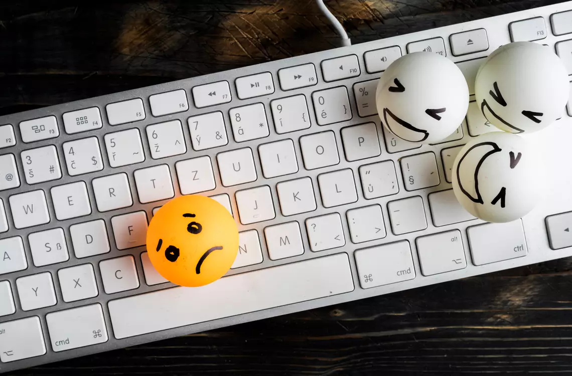 Une balle de pinp-pong posé sur un clavier avec un visage triste dessiné dessus et à côté trois autres balles qui ont des expressions moqueuses. 