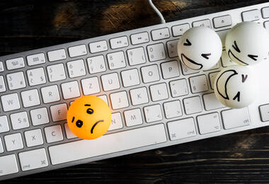 Une balle de pinp-pong posé sur un clavier avec un visage triste dessiné dessus et à côté trois autres balles qui ont des expressions moqueuses. 